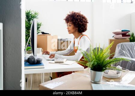 Donna afro che usa il computer mentre circondato da scatole di cartone dentro nuova casa Foto Stock