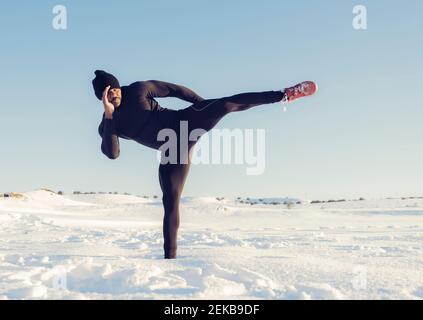 Atleta che pratica il kickboxing mentre in piedi nella neve nella giornata di sole Foto Stock