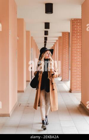 Giovane donna con una tazza da caffè riutilizzabile che attraversa il corridoio Foto Stock