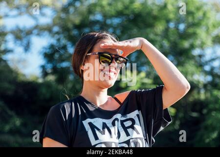 Primo piano di bella donna che indossa occhiali da sole che schermano gli occhi contro gli alberi nel parco Foto Stock