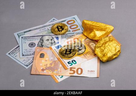 Concetto economico: Crypto valuta, denaro e oro sui mercati azionari globali. Tre lucenti bitcoin, due pezzi d'oro su alcune banconote IN EURO e dollari USA Foto Stock