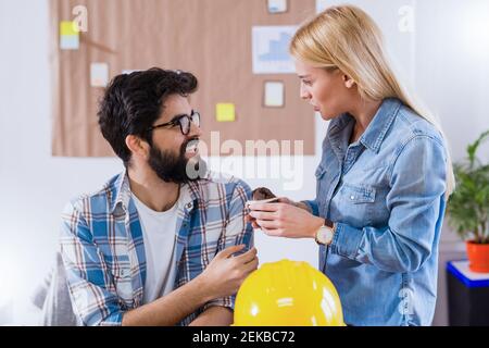 Due giovani colleghi felici che condividono i biscotti durante la pausa caffè in ufficio. Foto Stock