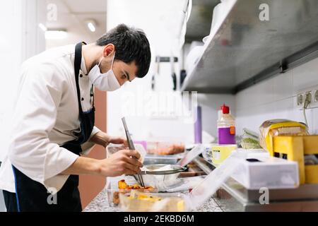 Chef maschile preparare cibo in contenitori di plastica in cucina a. Ristorante durante COVID-19 Foto Stock