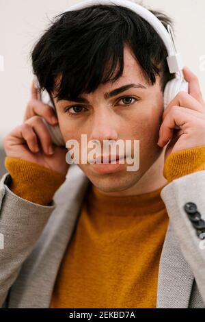 Giovane uomo che regola le cuffie mentre si sta in piedi all'aperto Foto Stock