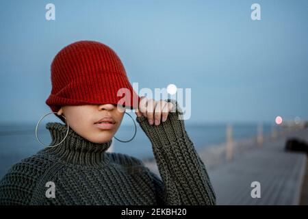 Donna che copre gli occhi con cappello a maglia mentre si sta in piedi  contro il cielo Foto stock - Alamy