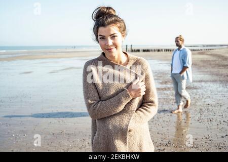 Giovane donna in piedi sulla spiaggia mentre il ragazzo cammina sullo sfondo durante il fine settimana Foto Stock