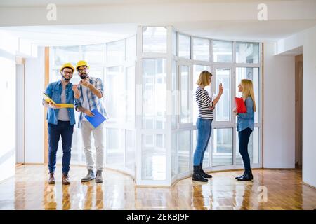 Gruppo di giovani architetti che camminano attraverso una stanza vuota e luminosa e discutono dei prossimi passi. Foto Stock