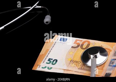 Concetto sanitario, assicurativo ed economico: Cinquanta banconote europee CON stetoscopio giacciono su sfondo nero. Sicurezza sociale Foto Stock