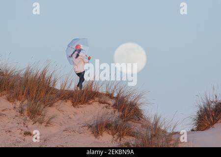 Giovane donna con ombrello su dune di sabbia contro il cielo durante crepuscolo Foto Stock