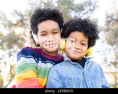 Fratello e sorella indossano cuffie sorridenti mentre si siedono insieme a. parcheggio Foto Stock