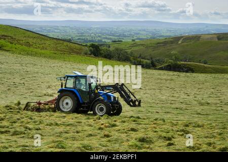 Fienagione di trattore (traino e traino del foraggio, allevamento di insilato di allevamento) in campo pascoli di campagna vicino Grassington, Yorkshire Dales, Inghilterra, Regno Unito. Foto Stock