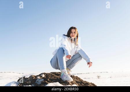 Giovane donna che sta fissando mentre accovacciando sulla roccia contro il cielo Foto Stock