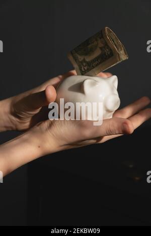 piccolo investitore di capretto che mette il suo primo dollaro noi in banca del piggy. soldi di risparmio del capretto per il concetto futuro. Foto Stock