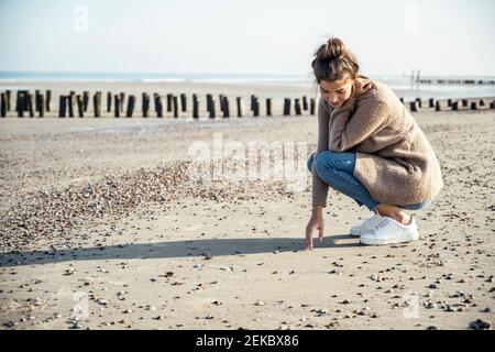 Giovane donna con posizione di squatting sulla sabbia in spiaggia Foto Stock