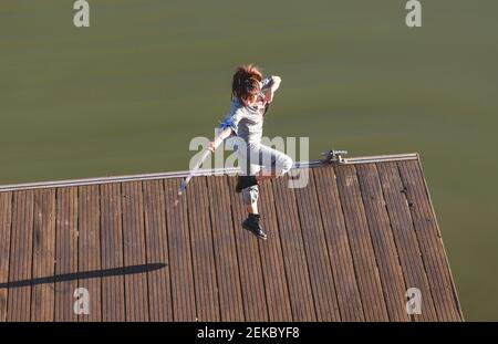 Atleta che esegue arti marziali acrobazie con la spada mentre salta sul lungomare durante il giorno di sole Foto Stock