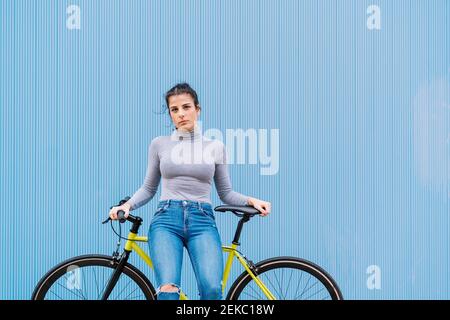 Donna mid adulta sicura seduta su fixie bike contro il blu parete Foto Stock