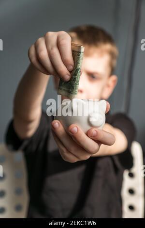 piccolo investitore di capretto che mette il suo primo dollaro noi in banca del piggy. soldi di risparmio del capretto per il concetto futuro. Foto Stock