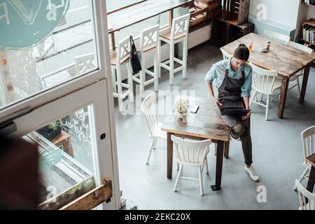 Cameriera femminile che usa il computer portatile mentre si siede sul tavolo al bar Foto Stock