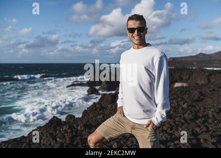 Sorridente turista maschile con le mani in tasca in piedi sul punto di vista dal mare a Los Hervideros, Lanzarote, Spagna Foto Stock