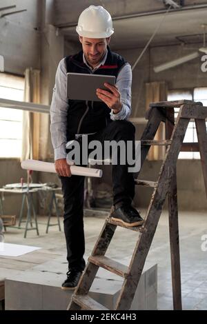 Ingegnere maschile che utilizza un tablet digitale mentre si sta in piedi nella costruzione a. sito Foto Stock