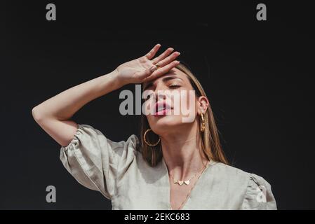 Primo piano di bella donna con gli occhi chiusi e mano sopra testa su sfondo nero Foto Stock