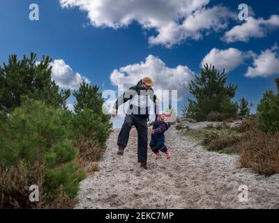 Il padre allegro solleva la figlia mentre si diverte sulla sabbia contro cielo durante l'inverno Foto Stock