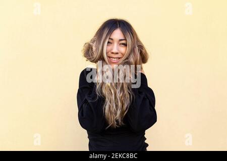 Felice giovane donna con mano in lunghi capelli in piedi contro sfondo beige Foto Stock