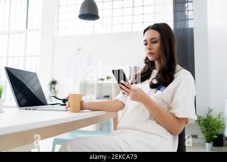 Giovane dottoressa che usa uno smartphone alla scrivania in clinica Foto Stock