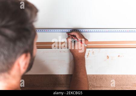 Giovane falegname maschio contrassegno su legno usando metro a nastro mentre lavori in officina Foto Stock