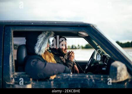 Giovane uomo che usa la radio CB mentre viaggia con un amico femmina in auto durante l'inverno Foto Stock