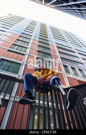 Giovane disabile con protesi di gamba seduta su ringhiera metallica contro l'edificio Foto Stock