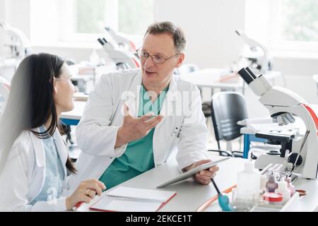 Insegnante e studente in cappotti bianchi che parlano e usano il tablet in laboratorio Foto Stock