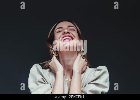 Donna allegra con mani in capelli su sfondo nero Foto Stock