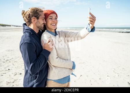 Ritratto di giovane coppia in piedi insieme sulla spiaggia e utilizzando smartphone Foto Stock