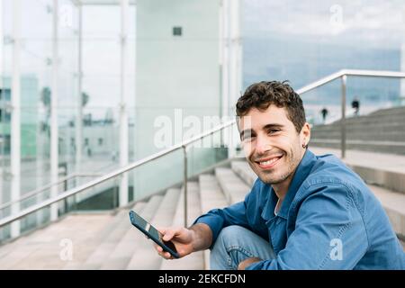 Ritratto di un giovane sorridente che tiene lo smartphone all'aperto Foto Stock