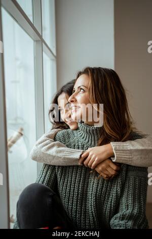 Madre e figlia felici che guardano attraverso la finestra mentre il giorno sogna insieme a casa Foto Stock