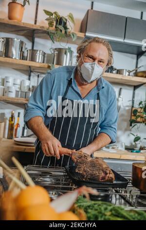 Esperienza maturata indossando maschera alla griglia tomahawk bistecca in frittura pan mentre in piedi in cucina Foto Stock