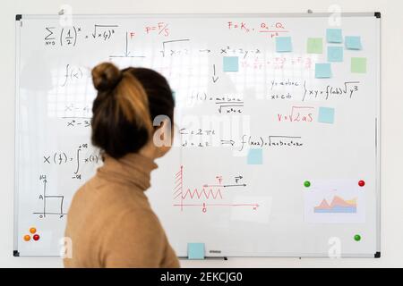 Donna che analizza la formula matematica scritta sulla lavagna in soggiorno Foto Stock