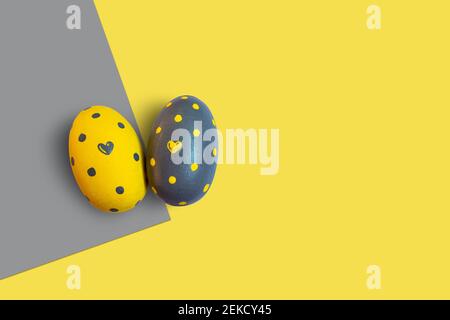 Pasqua in giallo illuminato e grigio estremo. Due uova decorate con cuori e puntini su uno sfondo bicolore. Foto Stock