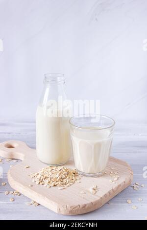 Latte di avena vegetale in una bottiglia di vetro e in una tazza di vetro su un tagliere di legno. Bevande sane, vegetarianismo. Vista laterale. Foto verticale Foto Stock