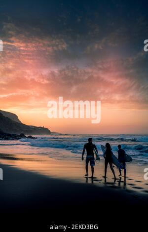 Surf gruppo di persone a piedi per l'oceano onde a. godetevi l'attività di sport acquatici di surf al tramonto - concetto di vita attiva e vacanze estive Foto Stock