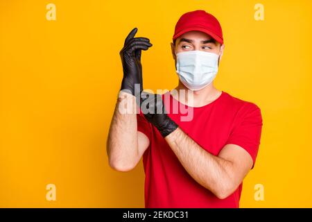 Primo piano ritratto di uomo di posta sano che indossa maschera mettendo guanti neri su mers cov prevenzione isolato su sfondo di colore giallo brillante Foto Stock