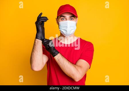 Primo piano ritratto di bello sano mailman indossare garza maschera mettere guanti neri sulla prevenzione di influenza canna fumaria isolati su giallo brillante sfondo a colori Foto Stock