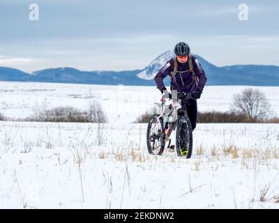 L'atleta adulto spinge una mountain bike attraverso la neve su un prato ghiacciato. Terreno duro, il motociclista non può guidare. Foto Stock