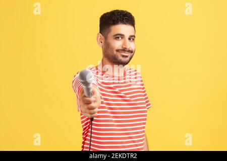 Reporter maschile bearded in t-shirt a righe con microfono, facendo intervista e chiedendo parere, discutendo argomenti importanti. Studio interno con isol di ripresa Foto Stock