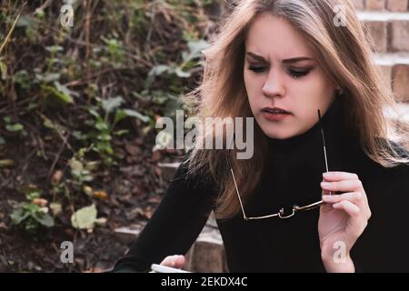 Ritratto di una donna seria concentrata che riceve cattive notizie, togliendo i suoi occhiali da sole dai suoi occhi. La donna è dumbfounded dalle informazioni lette Foto Stock