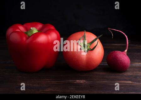 Pepe rosso, pomodoro, rafano rosso su un tavolo di legno scuro su sfondo nero. Foto Stock