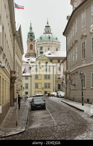 Centro storico di Praga coperto di neve con la Chiesa di San Nicola (Kostel svatého Mikuláše) in Piazza Malostranské, raffigurata da Via Sněmovní a Malá Strana (Città piccola) a Praga, Repubblica Ceca. Foto Stock