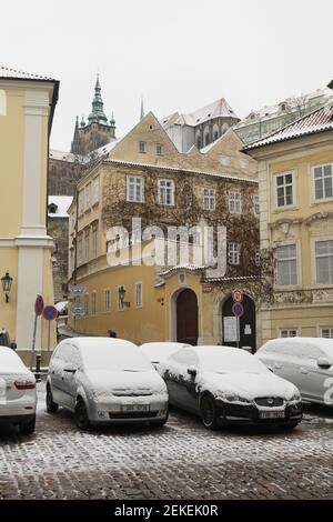 Auto parcheggiate coperte di neve in Piazza Valdštejnské (Valdštejnské náměstí) a Malá Strana (piccola città) a Praga, Repubblica Ceca. La Cattedrale di San Vito nel Castello di Praga è vista sullo sfondo. Foto Stock