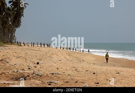 Gli abitanti del villaggio che condividono i pesci dalla rete di pesca della spiaggia Cape Coast Ghana. Vecchie reti da pesca fatte a mano tirate fuori di mare surf da gente del villaggio locale. Povertà. Foto Stock